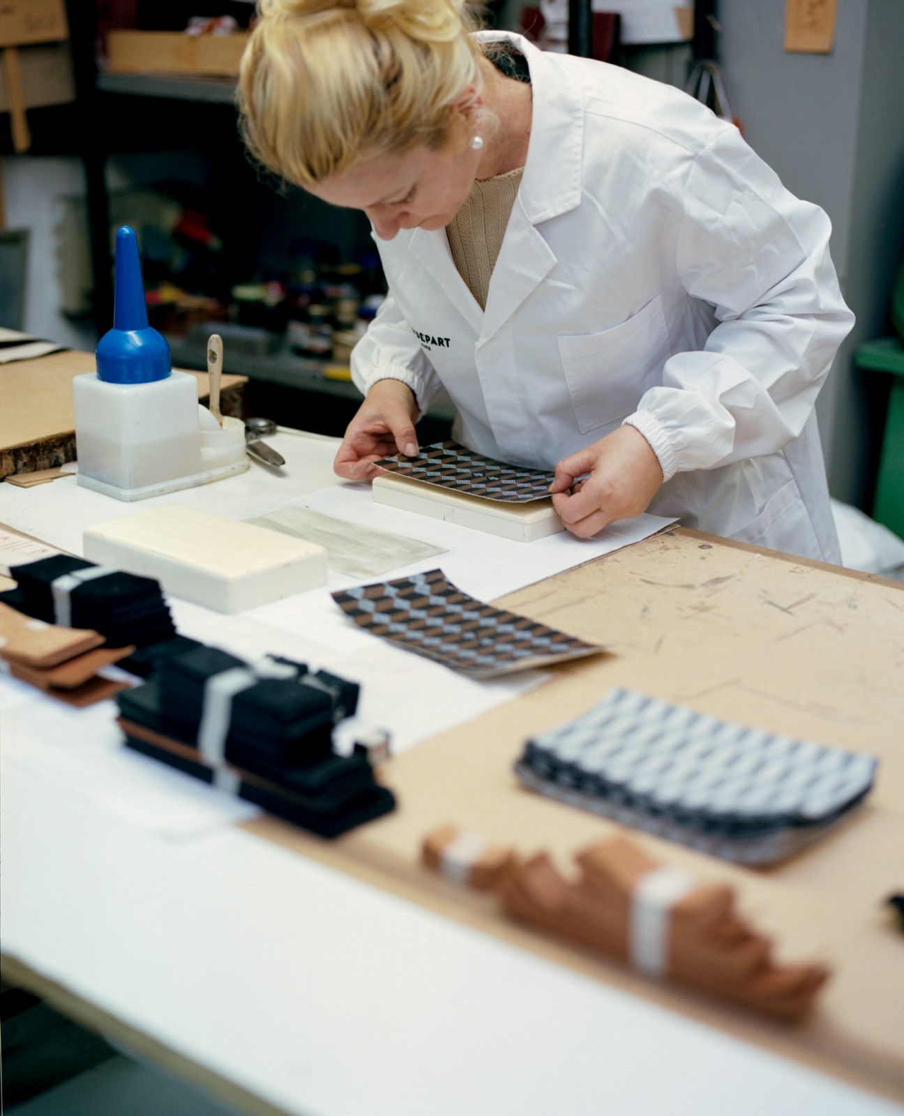 Craftsperson in white lab coat assembling metal and leather components at workbench in luxury workshop
