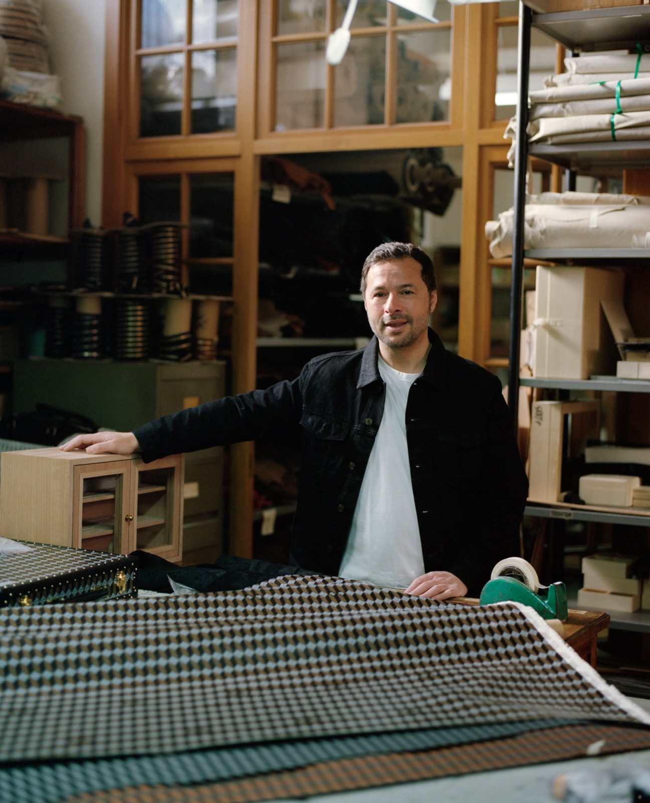 CEO Gianfranco Maccarrone standing in Au Départ's Milan atelier workspace with fabric and storage shelves