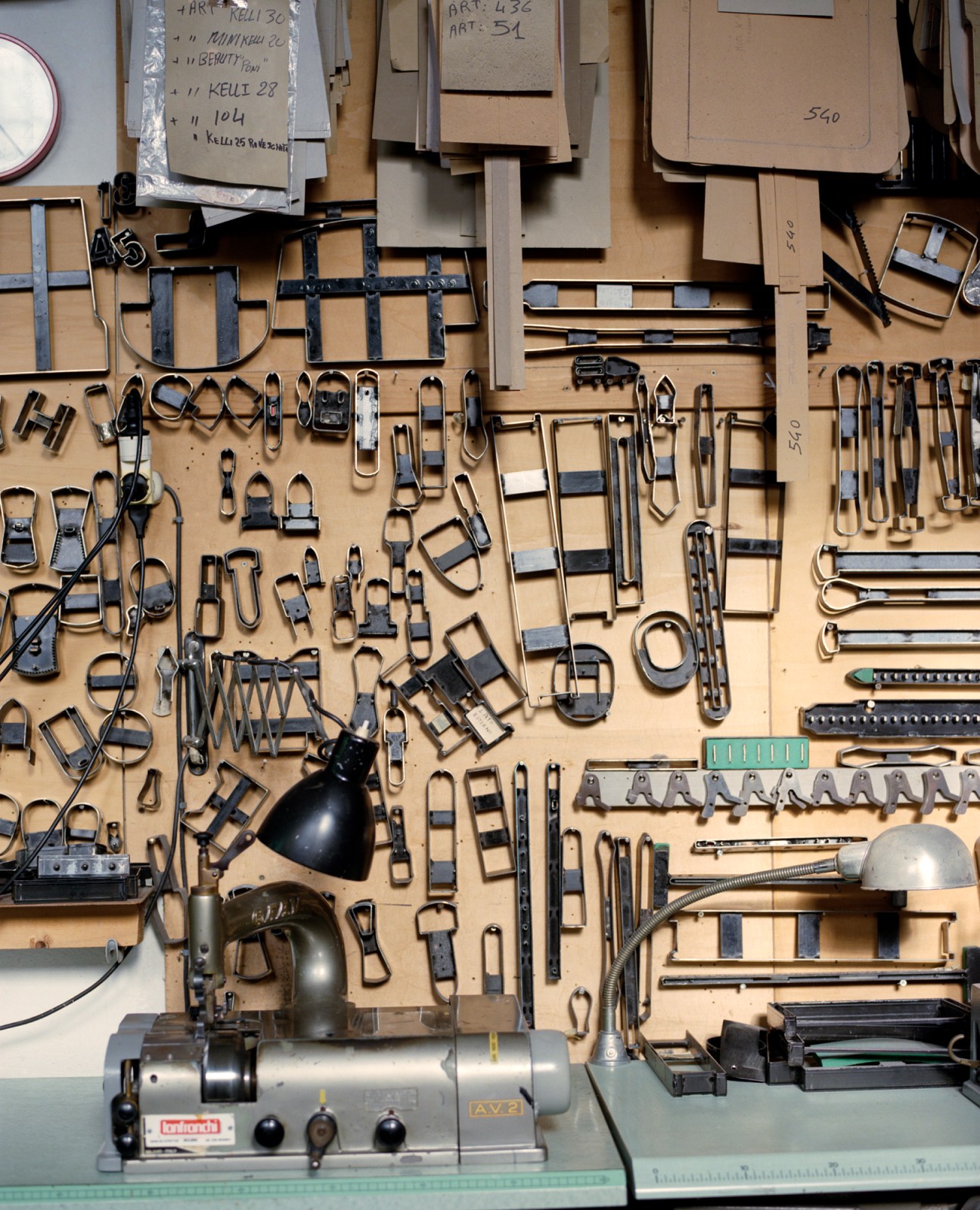 Wall display of metal hardware components including buckles, clasps, and fasteners in Au Départ workshop