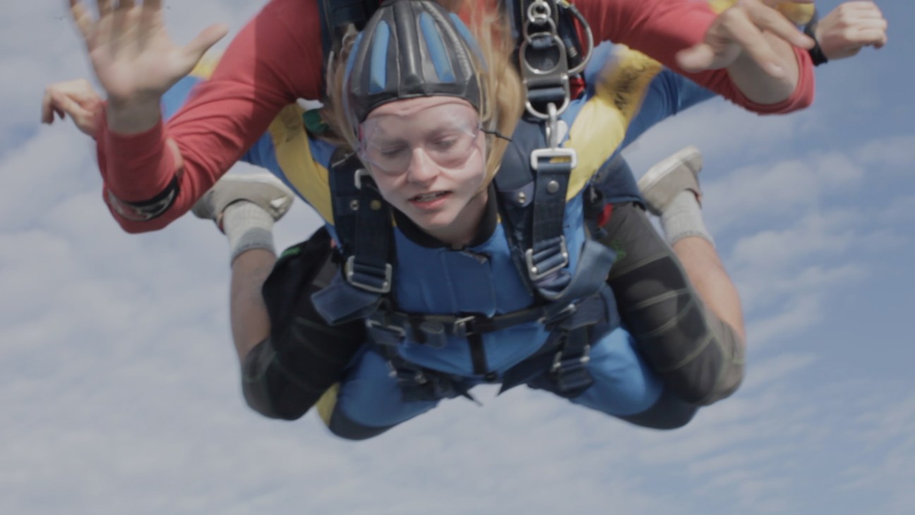 Two people skydiving in tandem against a cloudy sky background
