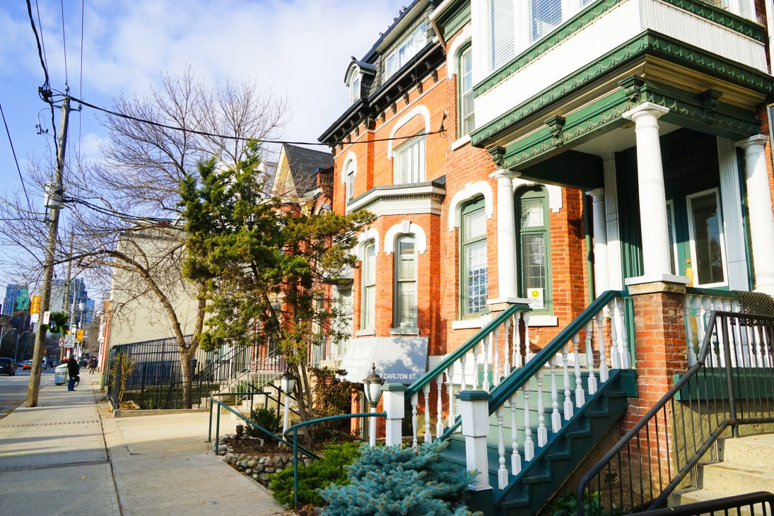 Victorian-era brick houses with green-trimmed porches and white columns line a Toronto street