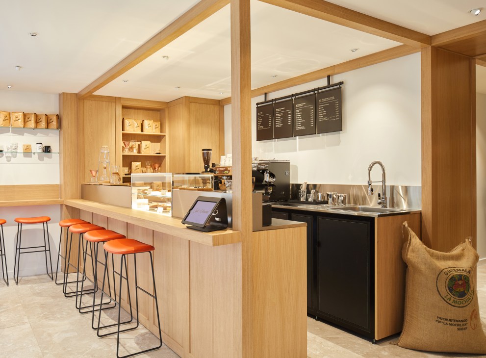 Maison Kitsuné café interior with wooden counter, orange bar stools, and coffee equipment.