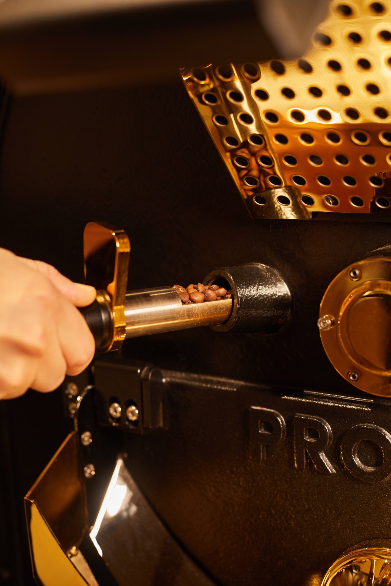 Hand operating a coffee grinder with roasted beans visible in the hopper at Maison Kitsuné café.