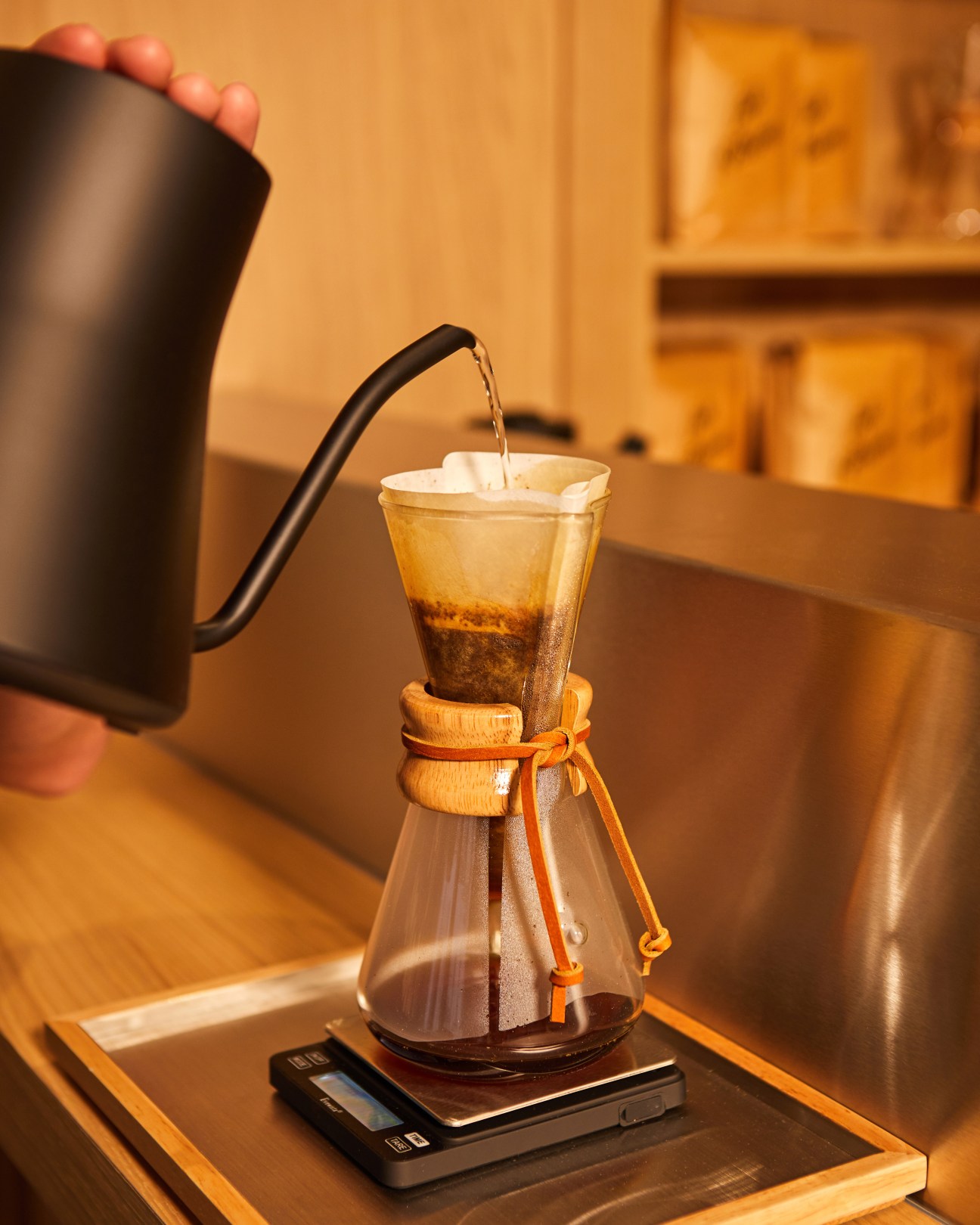 Hot water being poured from a black kettle into a glass Chemex coffee maker with wooden collar and orange tie.