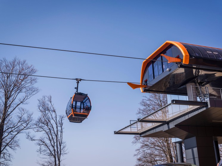 Modern cable car station with orange accents and glass facade against clear blue sky