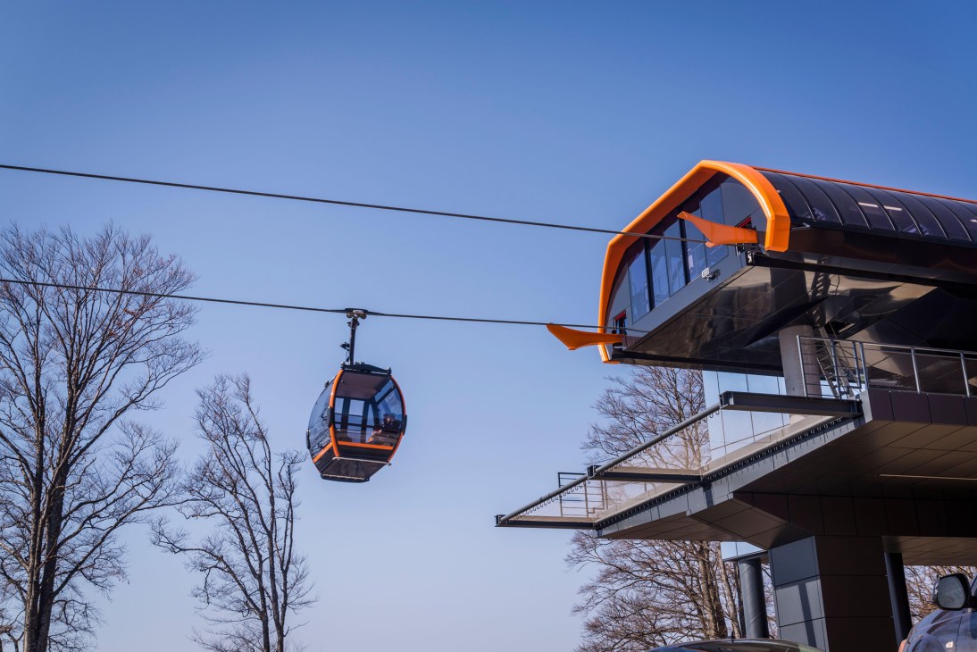 Modern cable car station with orange accents and glass facade against clear blue sky