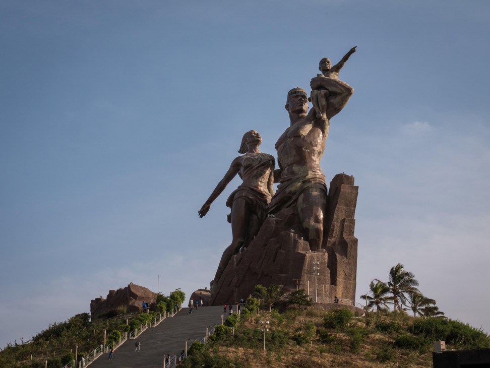 Large bronze monument showing multiple figures with outstretched arms against a clear sky