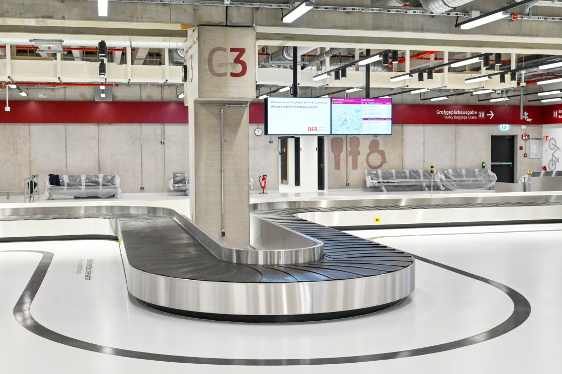 Berlin Brandenburg Airport baggage claim area with modern stainless steel carousel and signage.