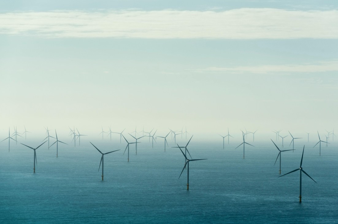 Offshore wind turbines standing in blue ocean water under cloudy sky