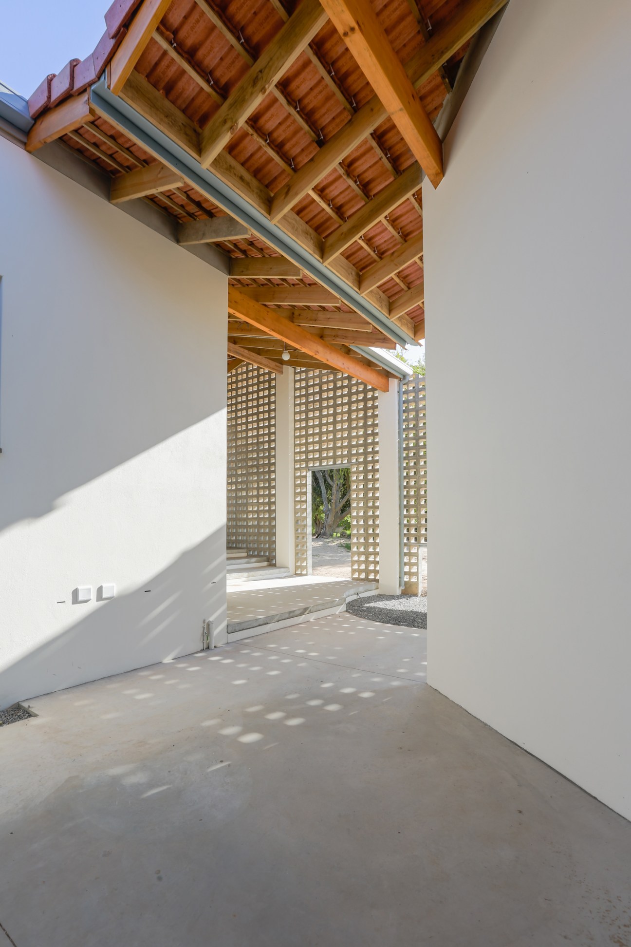 Covered outdoor space at Calling Academy extension with exposed wooden beam ceiling and perforated concrete screen walls
