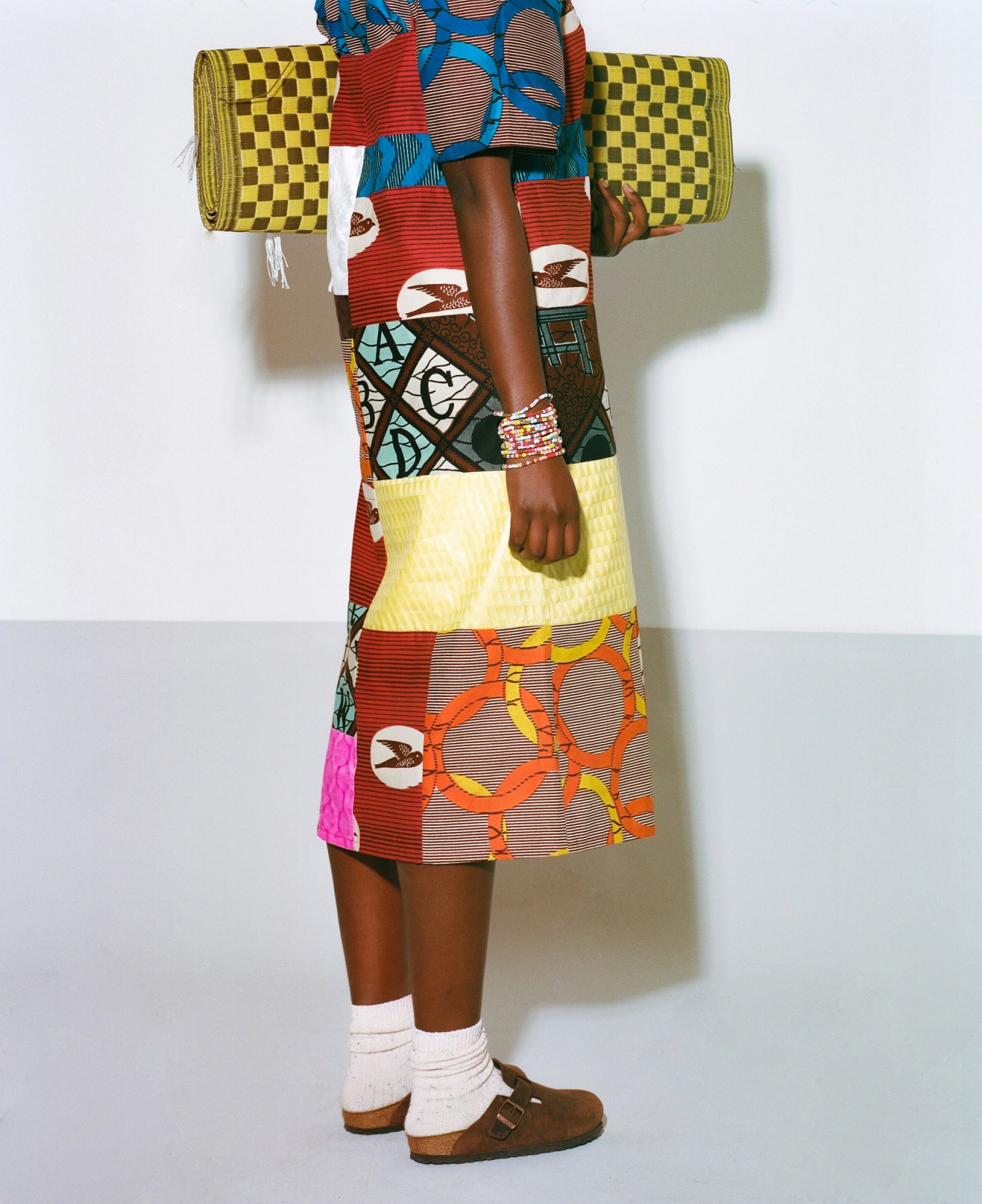 Model wearing colorful patchwork dress with African wax fabric patterns in various geometric designs