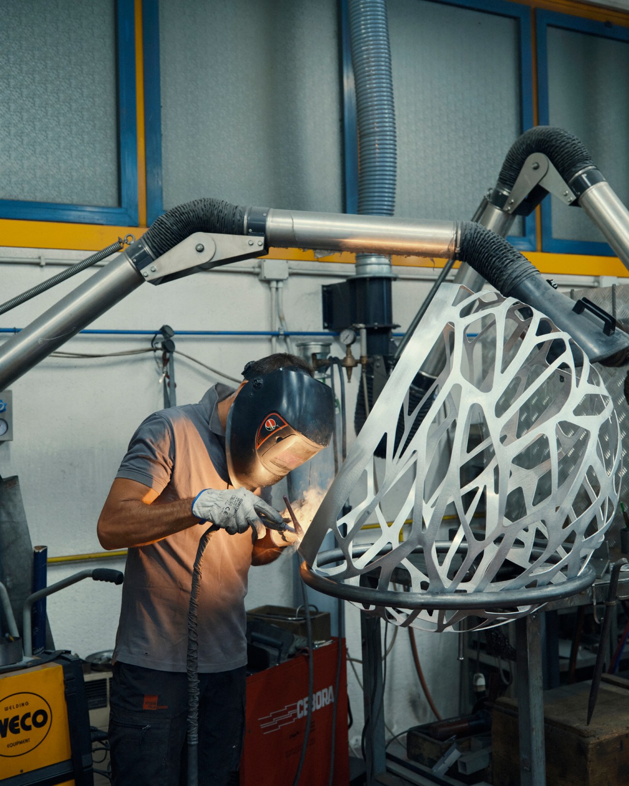 Worker in welding mask working on metal sculptural lighting fixture in workshop