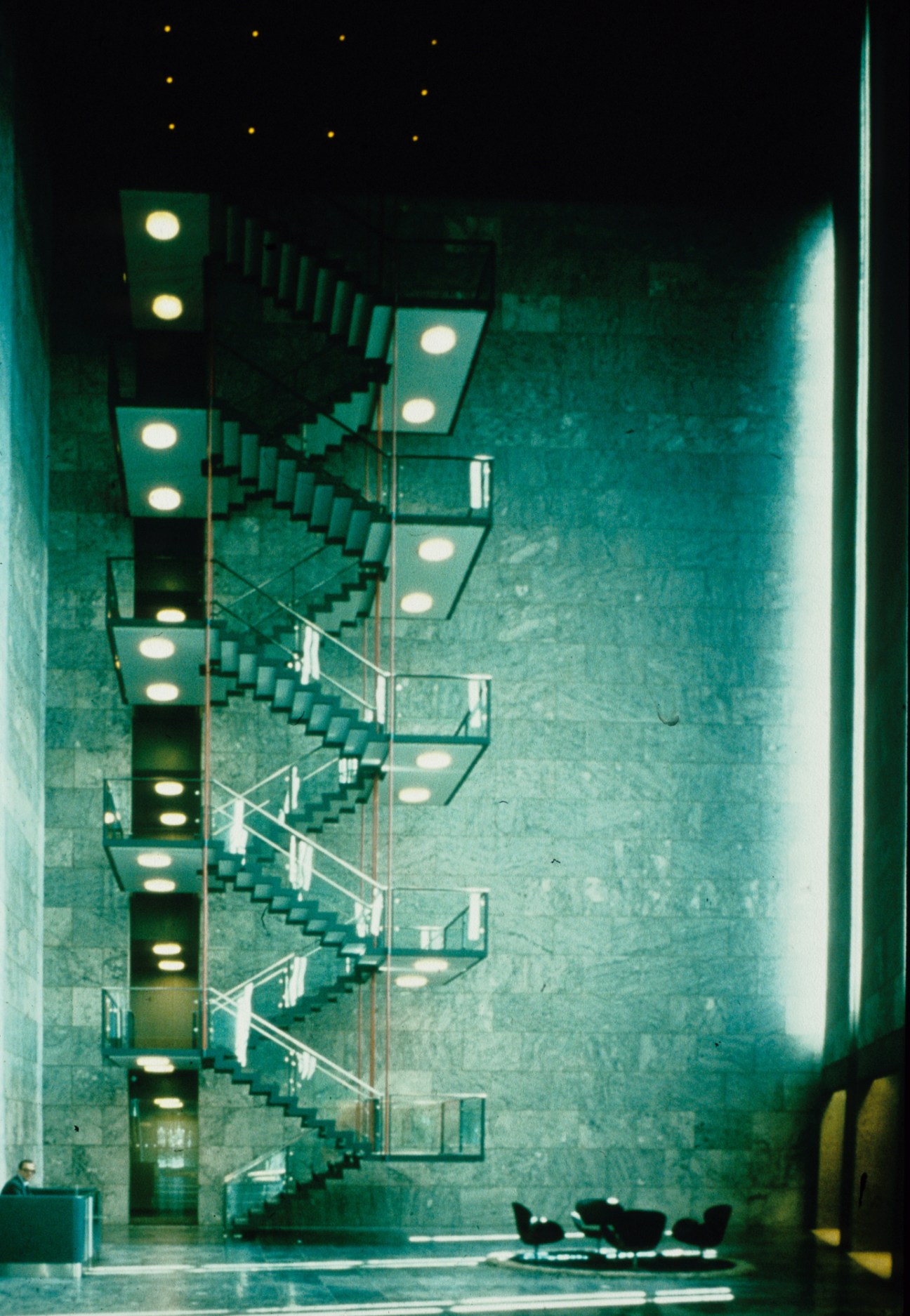 Interior of National Bank Copenhagen with illuminated wall fixtures and staircase, 1978.