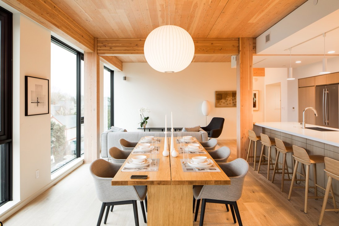 Interior of a wooden apartment with dining table, kitchen and living area showcasing timber construction.