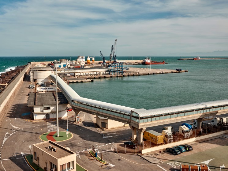 Elevated walkway and modern terminal building at Melilla's port with harbor and cargo ships in background