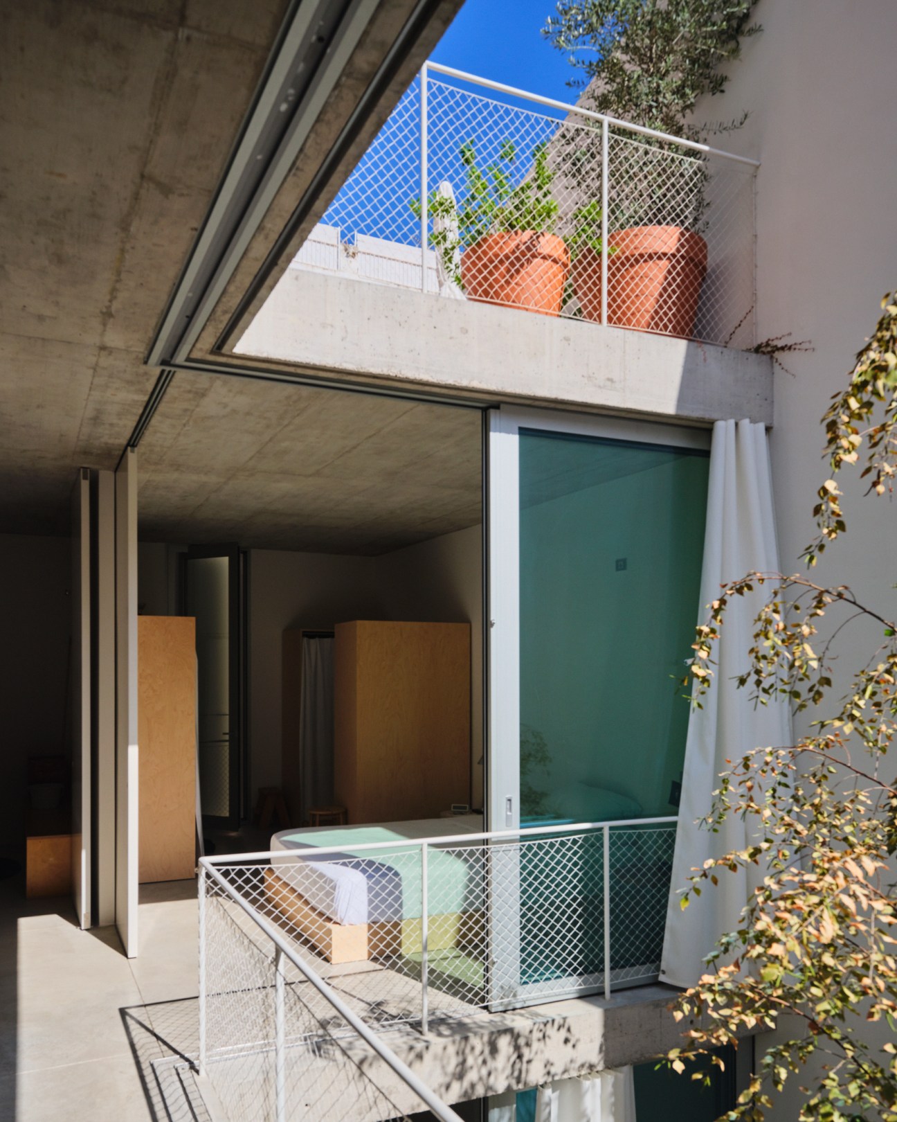 Multi-level concrete house with white mesh railings, terracotta planters, and floor-to-ceiling sliding glass windows