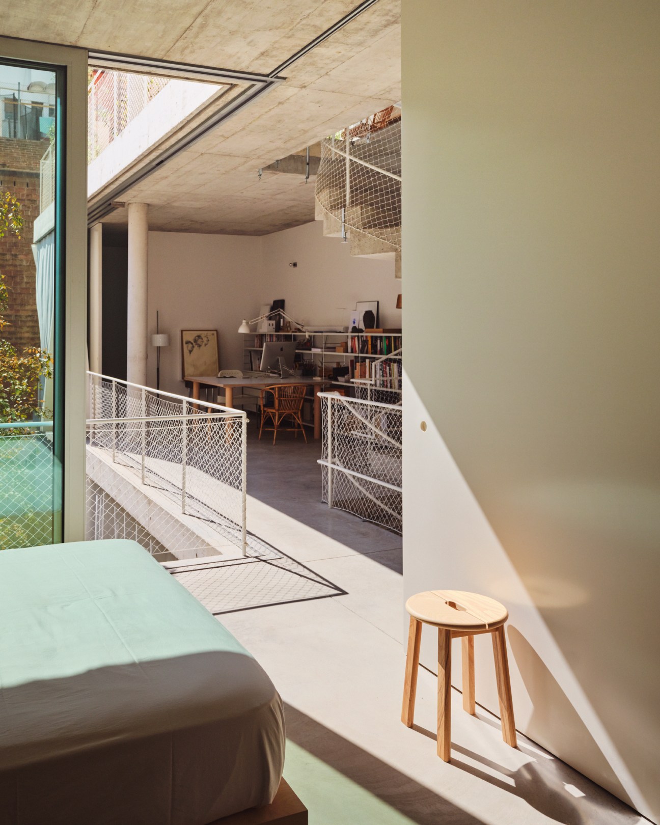 Multi-level interior with mesh railings, wooden stool, bookshelves and study area visible