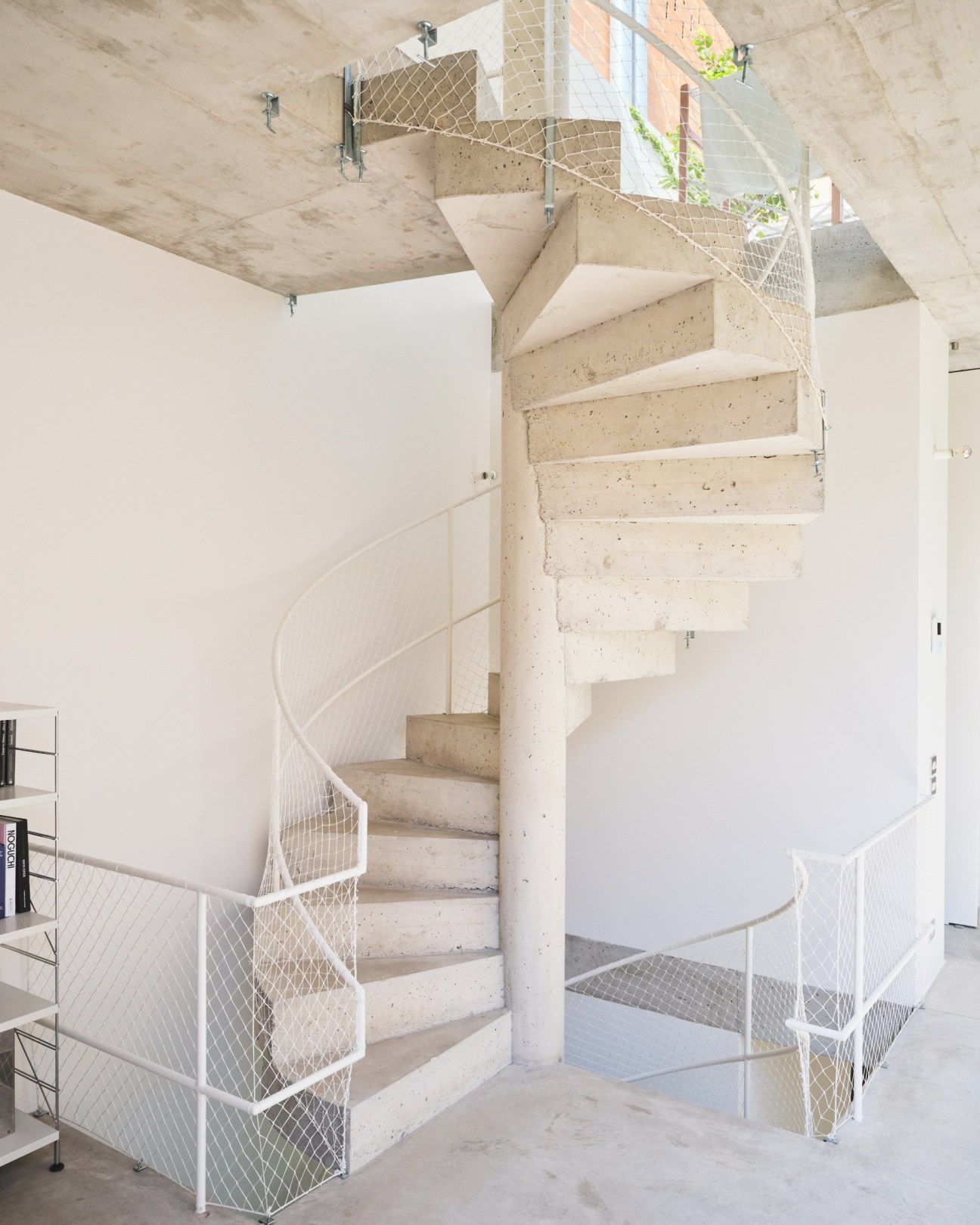 Sculptural exposed concrete spiral staircase with white metal mesh railings in modern home interior