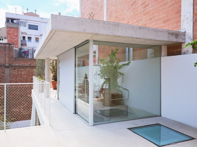 Modern roof terrace with glass pavilion, concrete surfaces, small pool and urban Barcelona backdrop