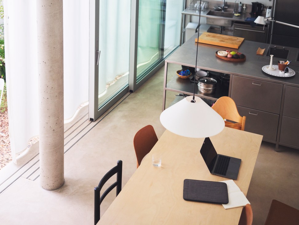 Modern dining area with wooden table, colorful chairs, pendant lamp, laptop and kitchen island in background