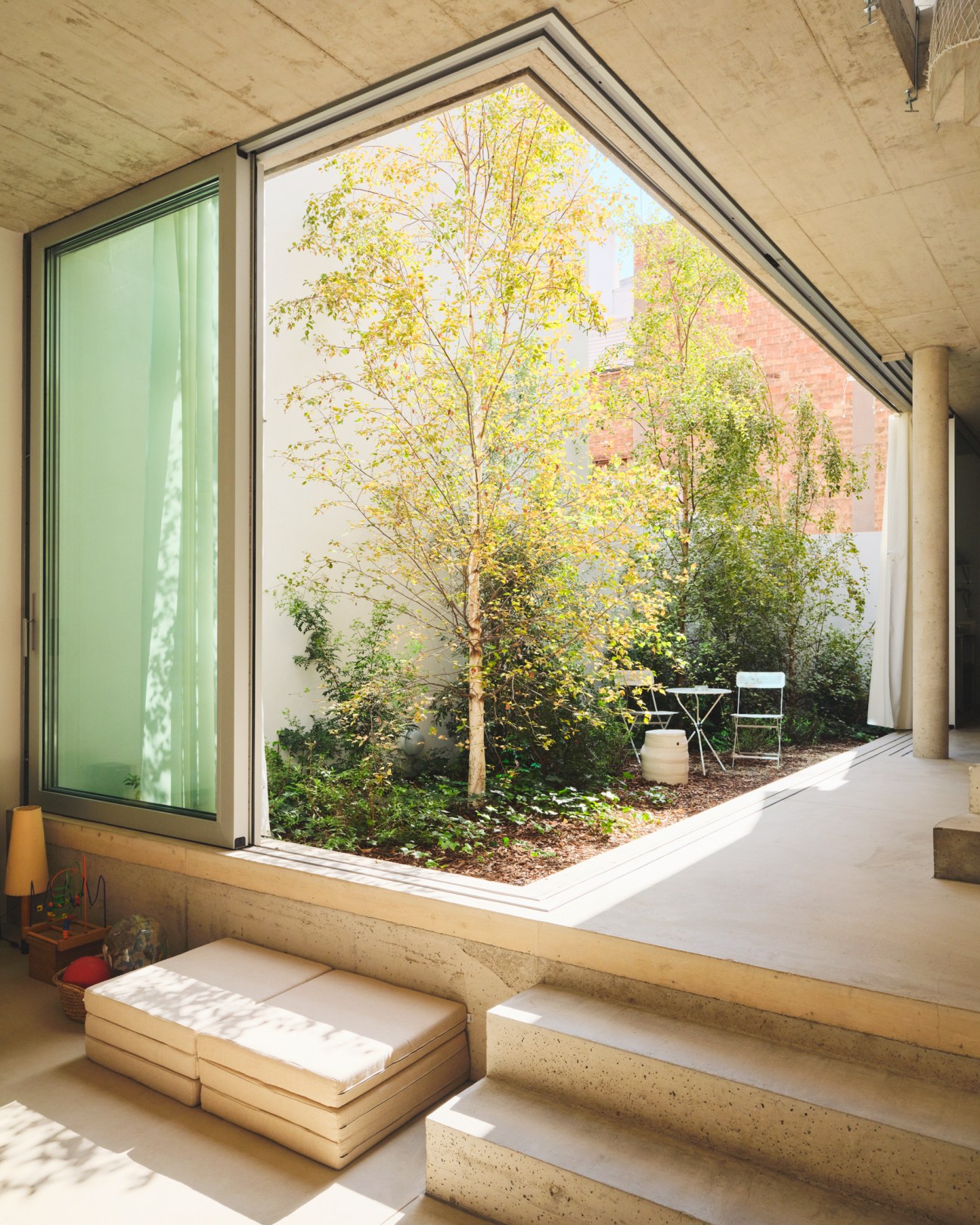 Modern interior seating area with floor-to-ceiling windows overlooking enclosed garden courtyard with birch trees