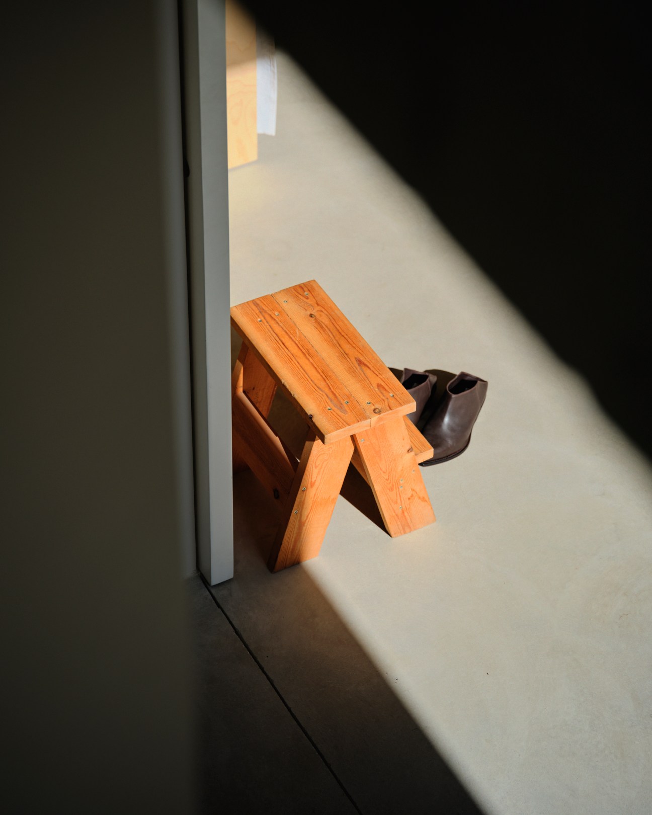 Sunlight casting diagonal shadows across concrete surfaces and an orange wooden stool