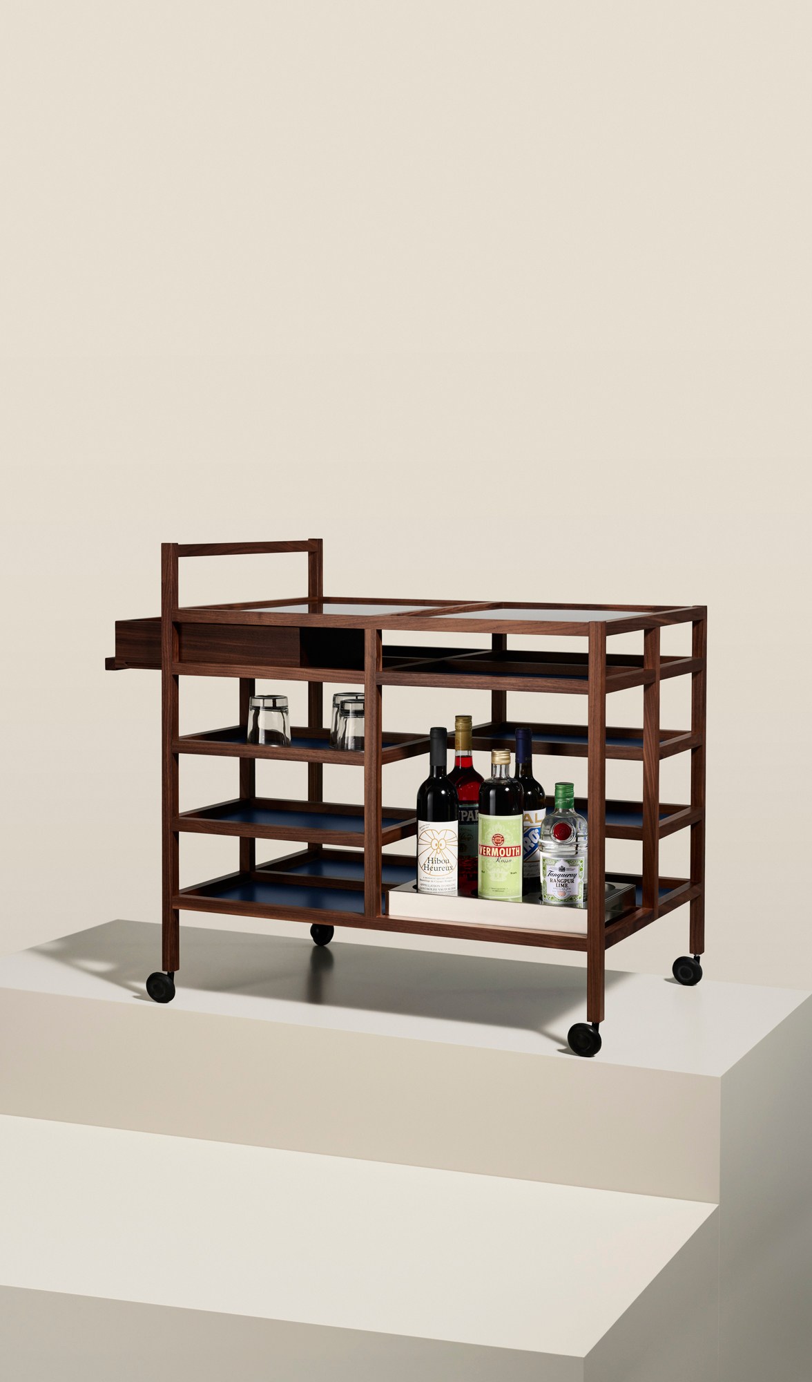 Bodil Kjaer 657 Serving Cart by Cassina featuring walnut wood frame with multiple shelves and bottles displayed on wheels