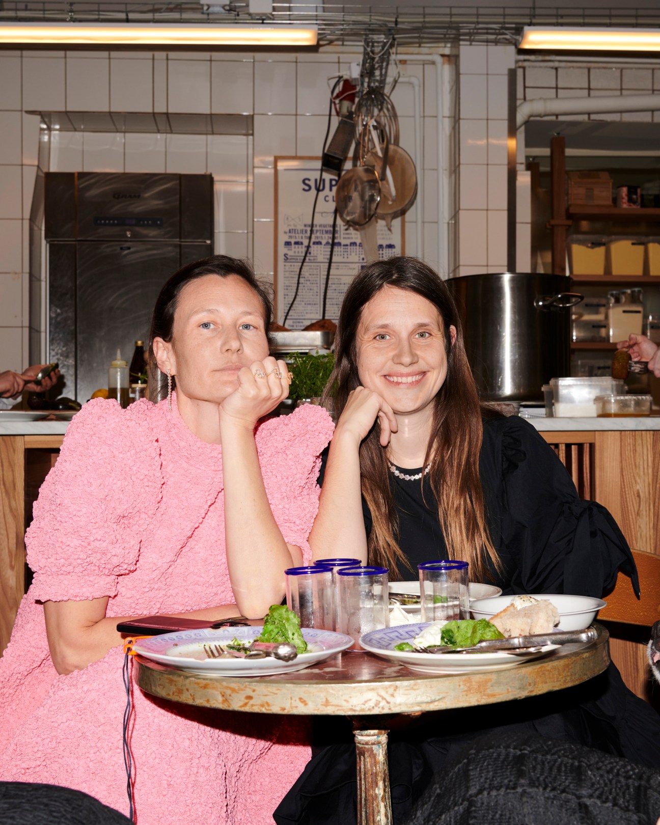 Two women sitting at a restaurant table having lunch with wine glasses and plates of food