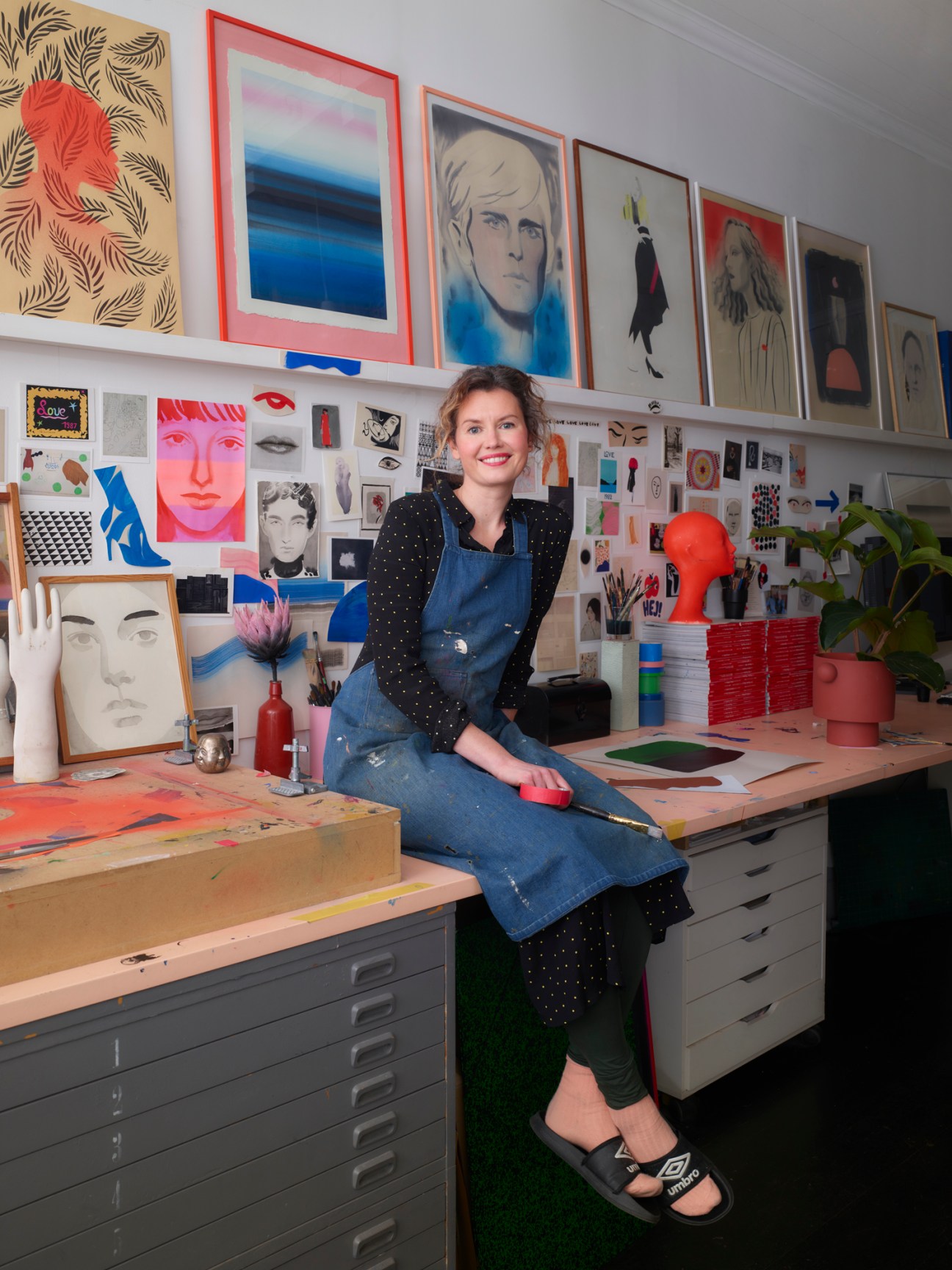 Cecilia Carlstedt sits in her art studio surrounded by framed illustrations and art supplies