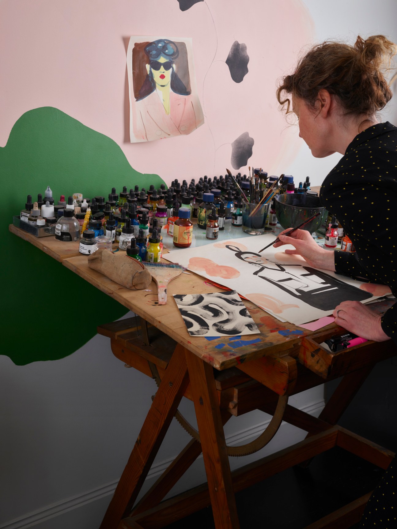 Cecilia Carlstedt working at her art table surrounded by paint bottles and brushes in her Stockholm studio