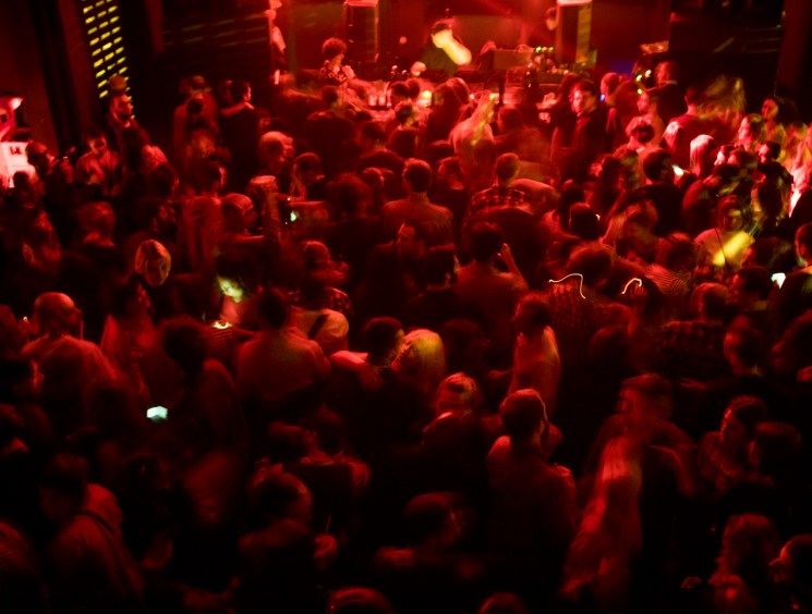 Crowded nightclub dance floor bathed in red lighting with people dancing under dramatic club lighting