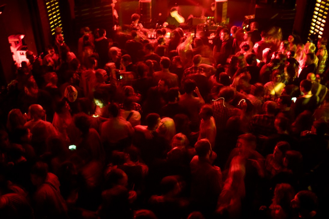 Crowded nightclub dance floor bathed in red lighting with people dancing under dramatic club lighting