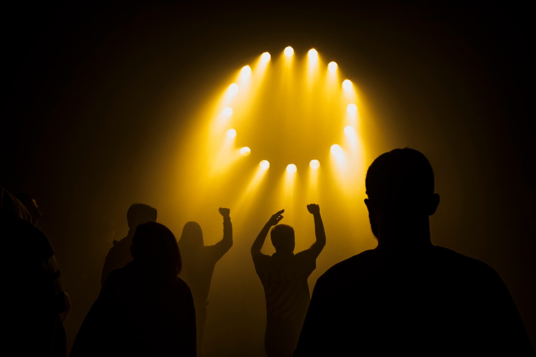 Silhouettes of concert audience with raised hands against dramatic yellow stage lighting