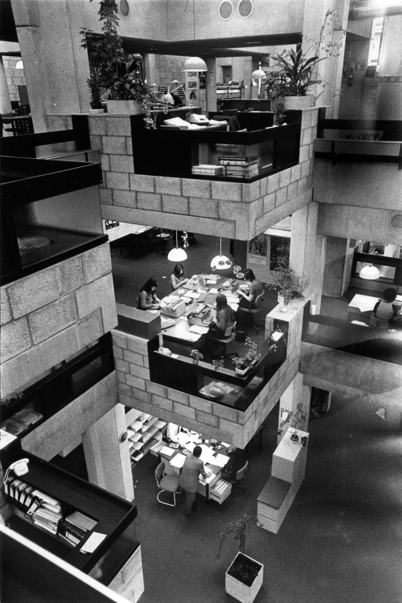 Overhead view of Centraal Beheer's multi-level interior with raw-brick work units at varying heights and employees at shared tables.