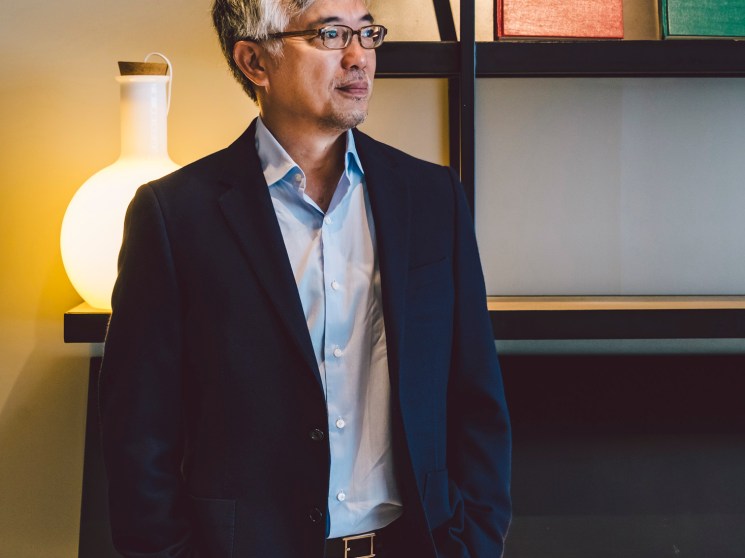 Tos Chirathivat, CEO of Central Group, stands in a modern interior with shelving and illuminated vessels.
