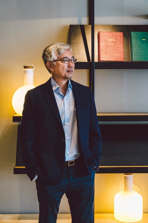 Tos Chirathivat, CEO of Central Group, stands in a modern interior with shelving and illuminated vessels.