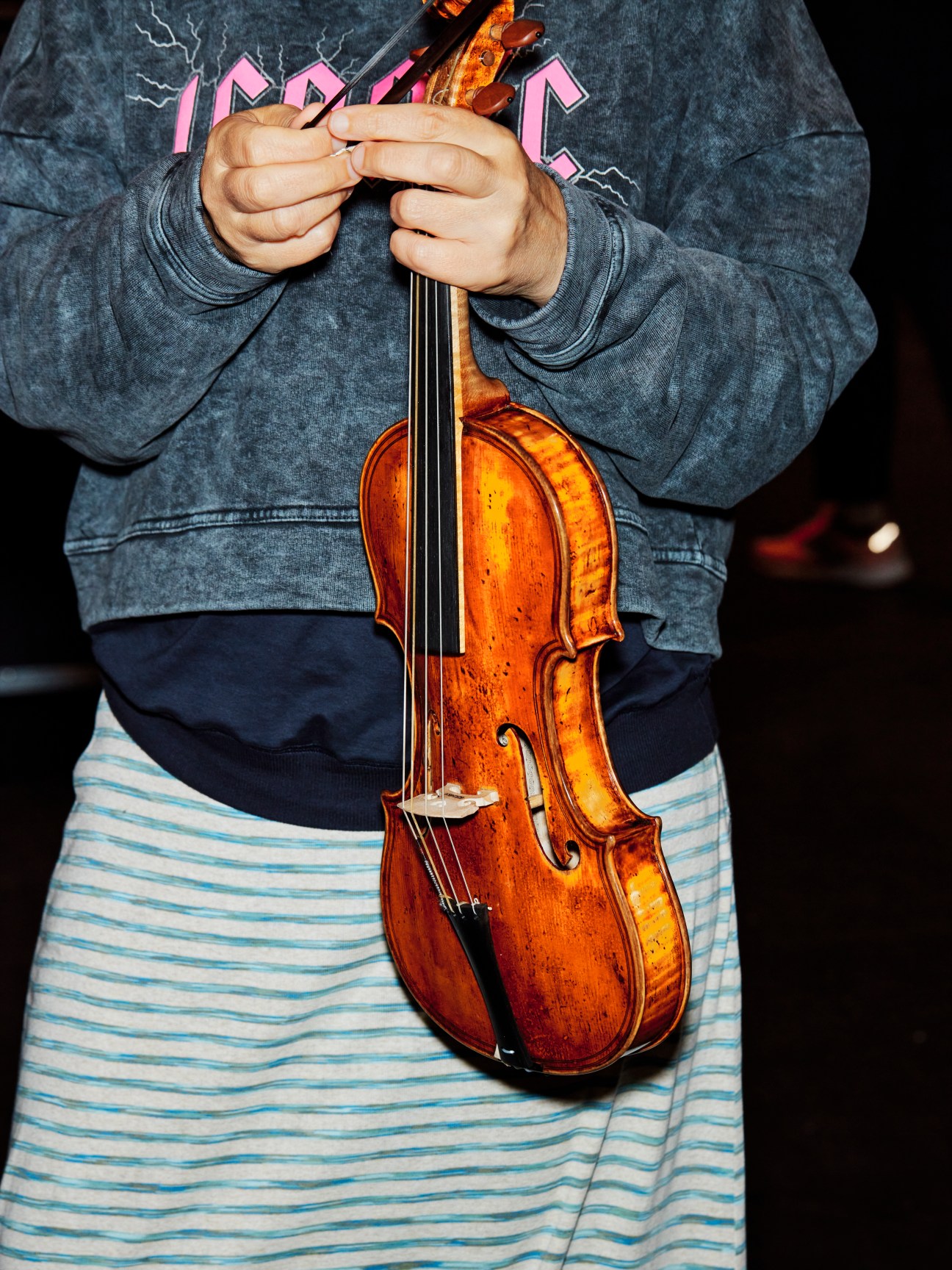 Person in gray sweatshirt holding wooden violin by the neck with both hands