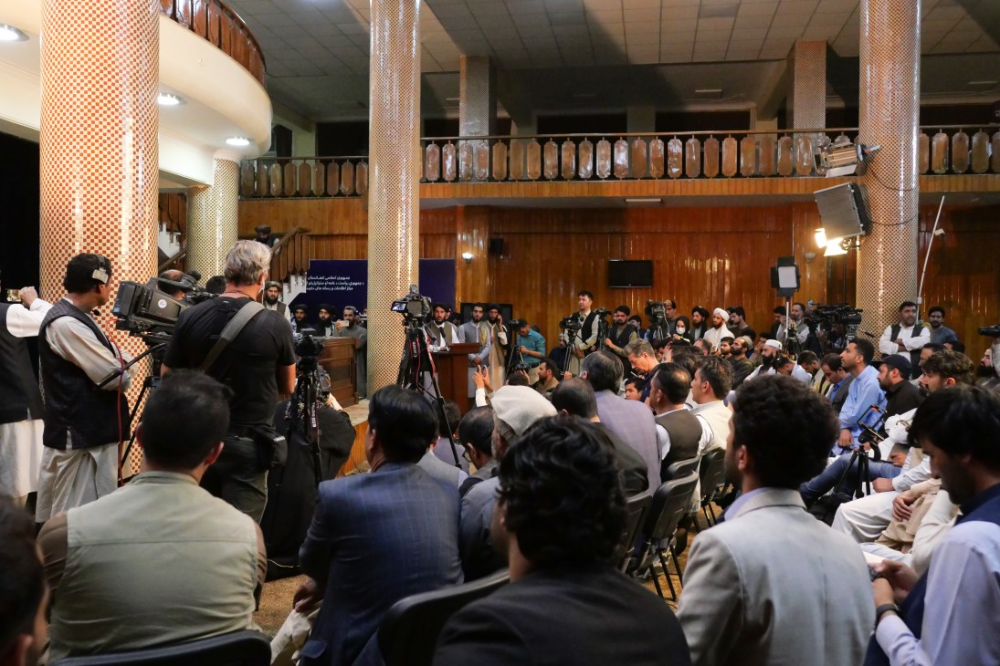 Taliban spokesperson Zabihullah Mujahid at podium during first public press conference in Kabul with media and journalists present