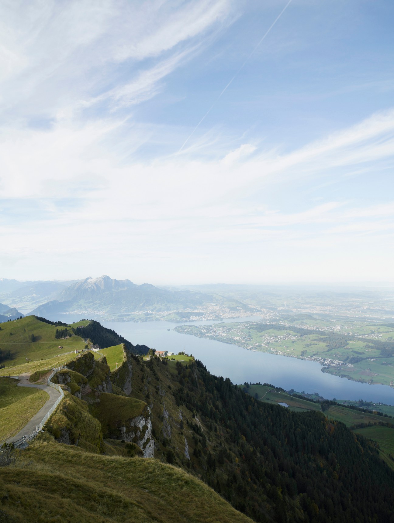 Alpine mountain landscape with lake and forested slopes under blue sky with wispy clouds.