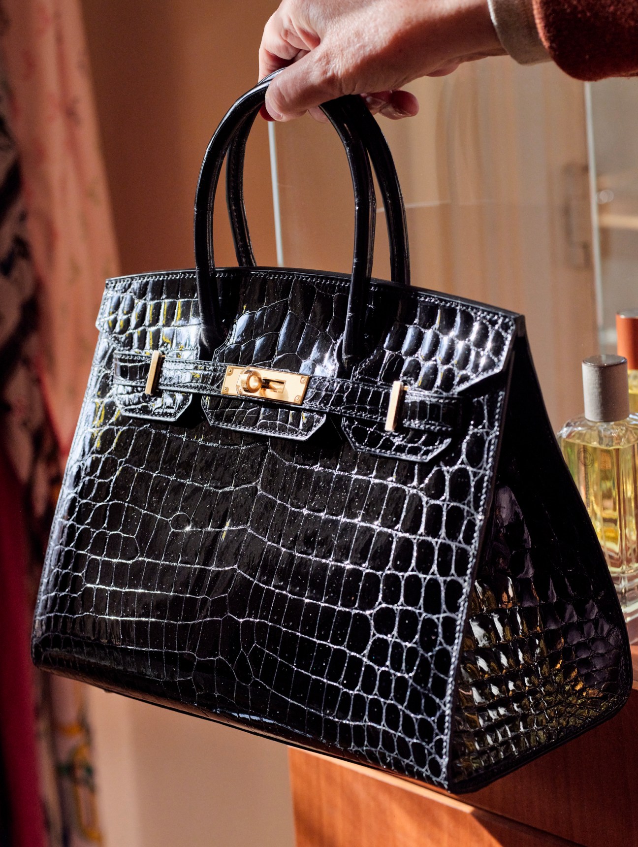 Black crocodile leather handbag with gold hardware being held by a person's hand.