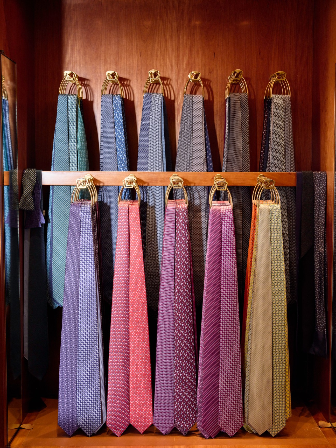 Display of colorful neckties hanging on wooden rods with gold fixtures against a warm wood-paneled wall.