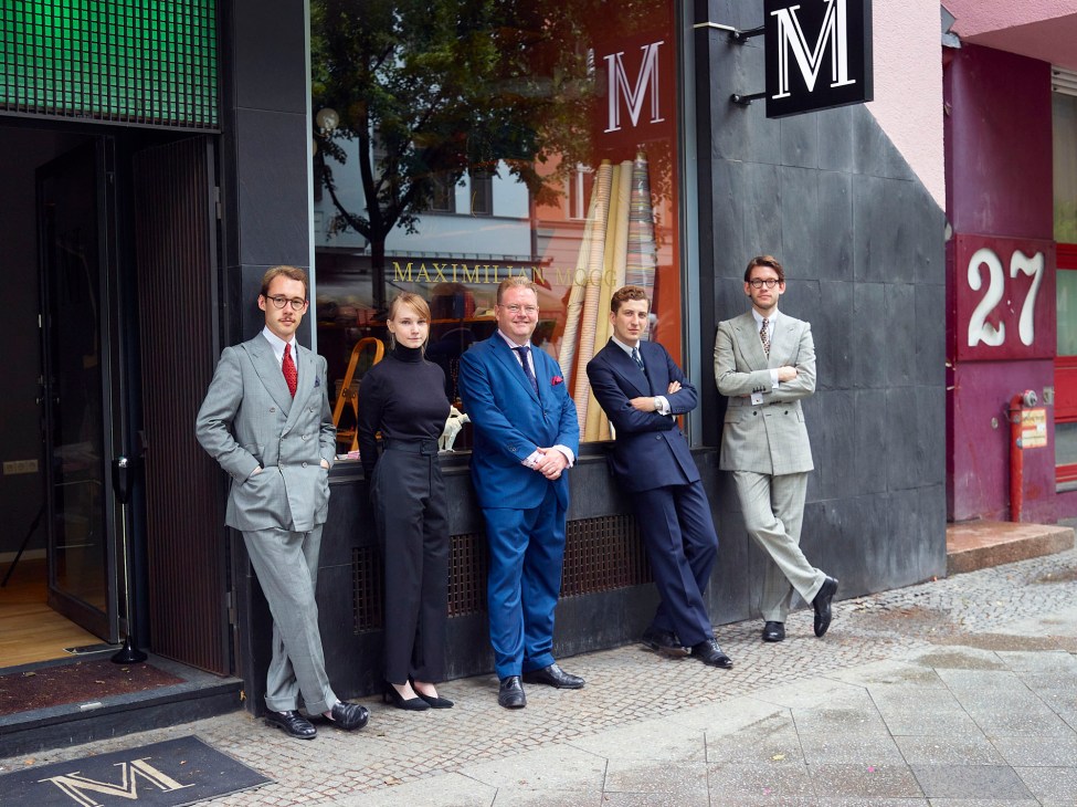 Five people in formal business attire standing outside a storefront with large M signage