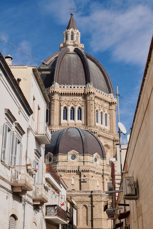 The Cathedral of San Pietro Apostolo in Cerignola, Puglia, with ornate stone facade and black dome topped by a white spire.