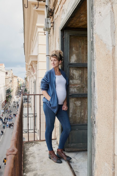 Pregnant woman stands on a Palermo balcony overlooking a street below