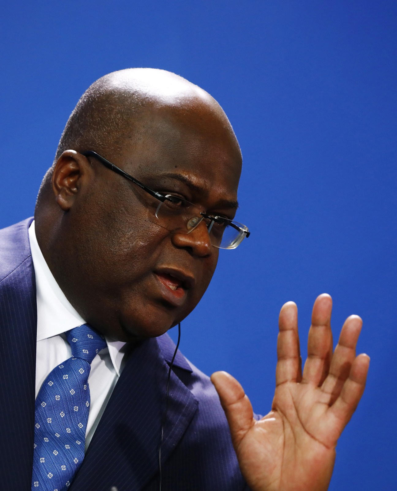 African man in blue suit and glasses speaking with raised hand