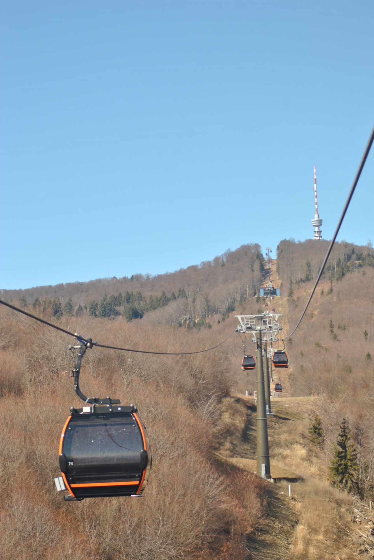 Black and orange cable car gondolas on mountain hillside with transmission tower visible on summit