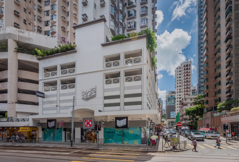 Modern white cinema building with glass windows and green signage on urban street with high-rise apartments