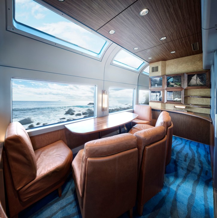 Green Car private room interior with tan leather seating, wooden table, and large windows showing ocean view