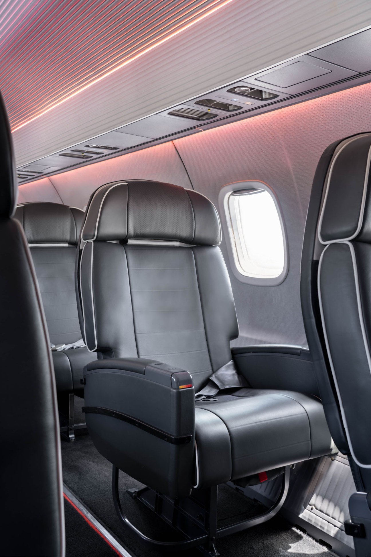 Premium airline seat with black leather upholstery, direct aisle access and ambient pink lighting in aircraft cabin