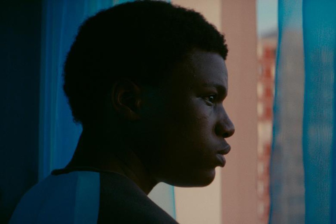A young Black man in profile, dramatically lit against blue tones in a scene from the film Gagarine